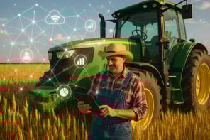 Farmer in a bright sunny wheat field leaning against a green tractor and holding a tablet high tech networking data symbols in the sky and field-1