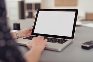 Businesswoman sitting at her desk navigating the internet on a laptop computer using the trackpad, over the shoulder view of the blank screen