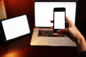 Closeup image of a female hand holding smartphone with tablet computer and laptop background