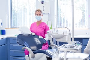 Dentist in mask looking at camera beside chair at the dental clinic