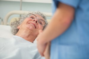 Elderly female patient looking up at nurse from hospital bed