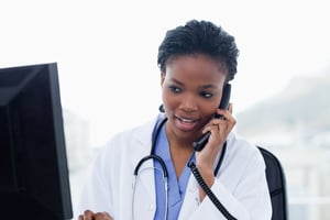 Женщина-врач разговаривает по телефону во время использования компьютера в своем кабинете