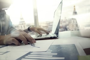 business documents on office table with laptop computer and graph financial diagram and man working in the background