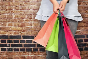 girl in bright colours holding shopping bags over a brick wall