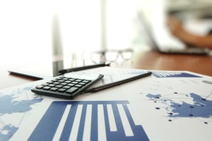 business documents on office table with calculator and digital tablet and man working in the background